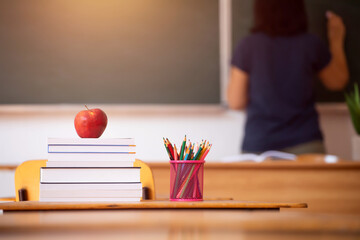 Pencils, apple and books, teacher and blackboard in the background. Education concept.