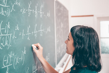Female student or teacher in the classroom writing on chalkboard mathematical equations