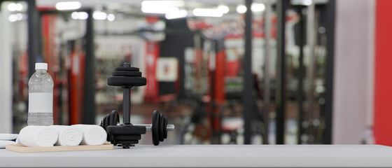 Dumbbells, drink bottle and towels on tabletop with space for product display over fitness gym...