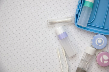 Rigid contact lens  on light background with holder, liquid, container, cleanser, tweezers and sucker
