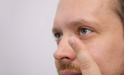 Fototapeta premium Man holds rigid lens on finger on light background. Fixing and use of contact lenses