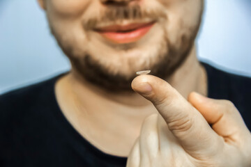 Rigid lens on finger on dark background with holder, liquid, container, cleanser and sucker. Contact lenses