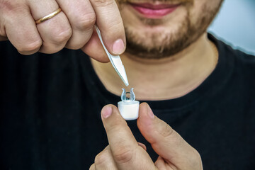 Rigid lens on finger on dark background with holder, liquid, container, cleanser and sucker. Contact lenses