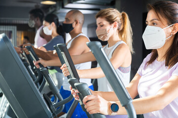 Portrait of sporty woman in protective face mask exercising on elliptical cross trainer in gym