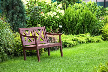 Beautiful landscape design of the house territory. A bench on a green lawn with flowering ornamental plants