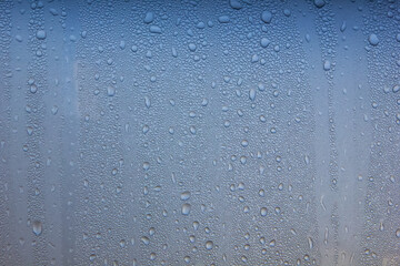 Water drops of morning dew on window glass, smooth surface. Set of condensation droplet  on a blue Background. Texture, abstract background, backdrop