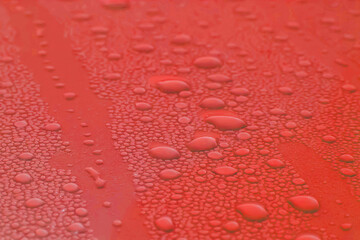 Water drops of morning dew on a  car hood, smooth surface. Set of condensation droplet  on a red background. Texture, abstract background, backdrop