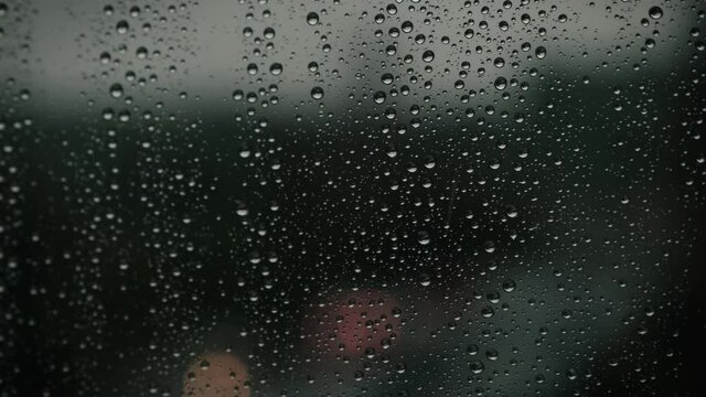 Close-up of water droplets on glass, Raindrops strike a window pane at twilight.
