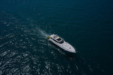 The yacht is fast moving on dark water. Large white yacht on the water in motion top view. Luxury motor boat on dark blue water aerial view.