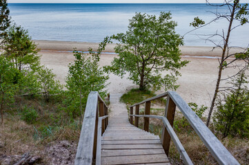 Fototapeta na wymiar Footbridge over a dune at the beach in Latvia. Baltic Sea. Wooden steps leading to white sand beach. Summer landscape. Evazu Nature Trail.