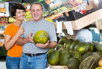 Fototapeta premium Happy man and his wife are choosing ripe melon in the fruit store