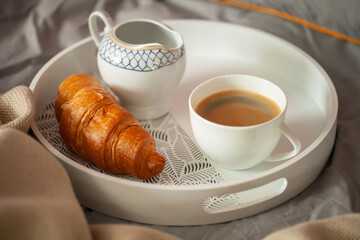 Breakfast on a tray in bed. Coffee, croissant and milk. Romantic concept
