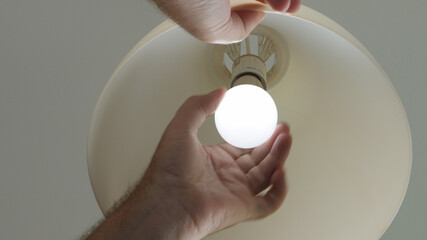 Electrician's Hand Changing a Led Light Bulb in a Lamp.