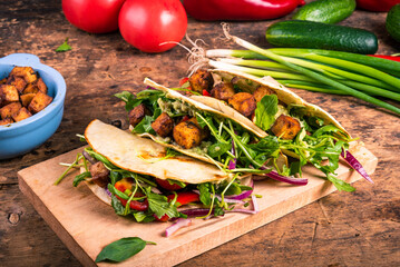 Vegetarian tacos - tortillas with vegetable salad and fried tofu on a wooden board on a table with ingredients, close-up