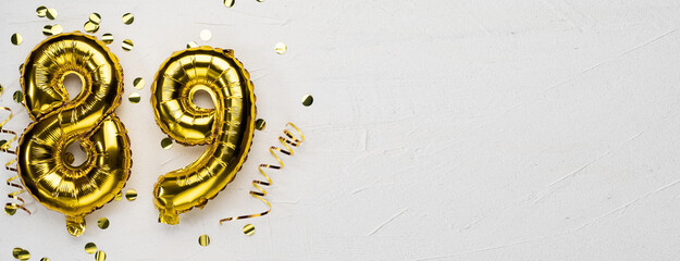 golden foil balloon number eighty nine. Birthday or anniversary card with the inscription 89. gray concrete background.