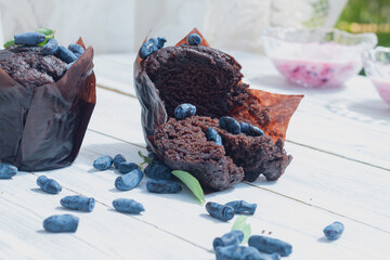 Delicious chocolate muffins with honeysuckle berries on a white wooden background
