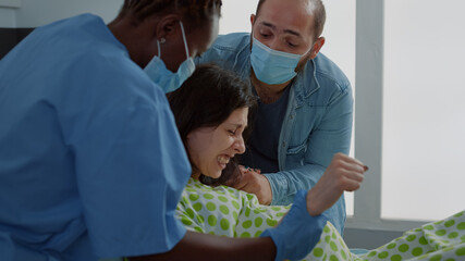 Young woman in labor giving birth to baby in hospital ward with support from husband and african...
