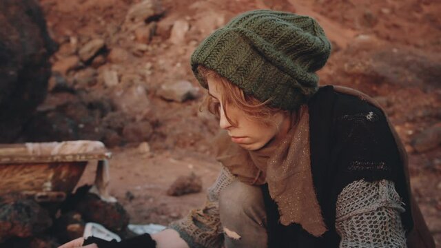 Close up shot of young woman in old clothes taking off vintage record player, vinyl record and smoke bombs from wooden box at campsite in dystopian world