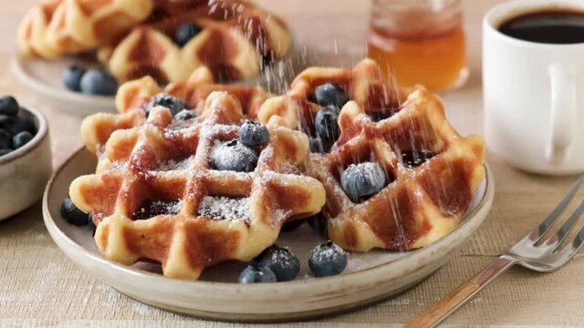 Sift confectioner's sugar on belgian waffles in slow motion. Sweet breakfast food, closeup view of yummy crispy waffles