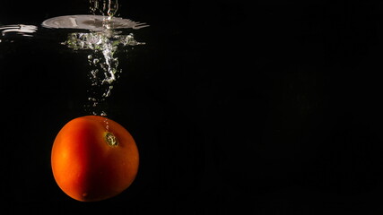Ripe tomato falls deeply under water with a big splash