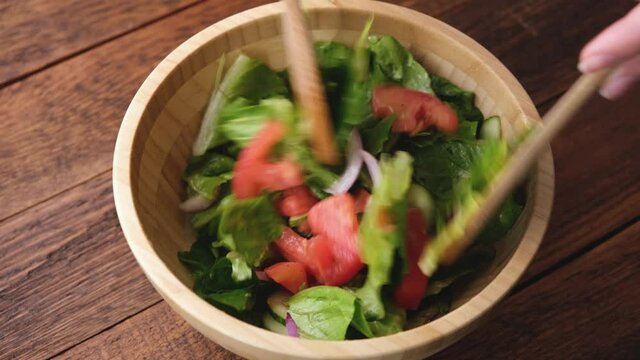 Tossing healthy salad with olive oil salad dressing or vinaigrette. Vegan vegetable salad bowl