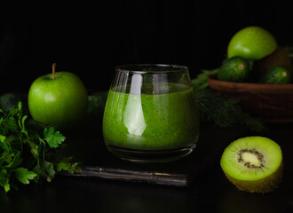 Green smoothie in a glass glass on a black background. Kiwi, apples,cucumbers and greens. Cooking healthy food.