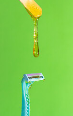 Sugar paste for hair removal against a razor. Sugaring paste drips on a razor on a green background. The concept of epilation, spa, body care