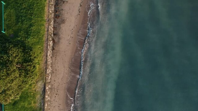 Birds eye aerial footage over a New Zealand shore with blue ocean waters. Parallel to the shore