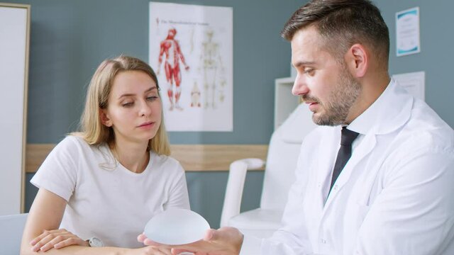 Plastic surgeon showing tho his female patient breast implant samples for her future surgery. Professional and famous surgeon working in respectable clinic