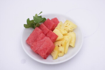 fresh red watermelon and yellow pineaple slices served with green mint leaves in the white plate.