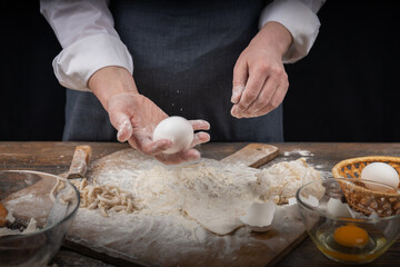 Women's hands, flour and dough. A woman in an apron cooking dough for homemade baking, a rustic home cozy atmosphere, a dark background with unusual lighting.