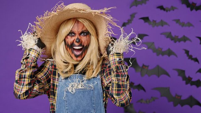 Sad angry mad young woman with Halloween makeup mask wears straw hat scarecrow costume scream swear shout call out gesticulating with hands isolated on plain dark purple background studio portrait