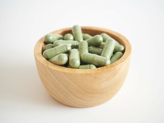 Green herbal powder capsules or andrographis paniculata in wooden bowl on white background. concept of drug treatment for covid-19. closeup photo, blurred.