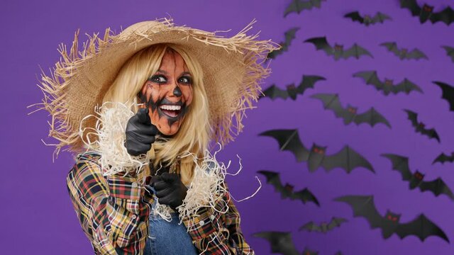 Confident leader young woman with Halloween makeup mask wears straw hat scarecrow costume point index finger camera on you motivating encourage isolated on plain dark purple background studio portrait