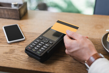 cropped view of customer paying with credit card in cafe