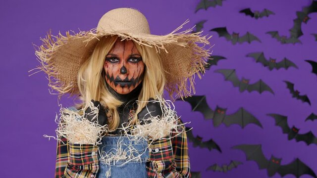Scary young woman with Halloween makeup mask wears straw hat scarecrow costume looking camera stroking hair isolated on plain dark purple background studio portrait. Celebration holiday party concept