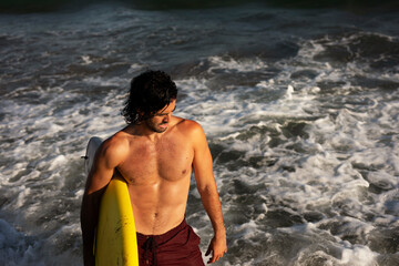 Fototapeta premium Portrait of handsome surfer with his surfboard. Young man with a surfboard on the beach.