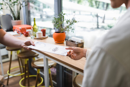 cropped view of waiter giving menu to client in cafe