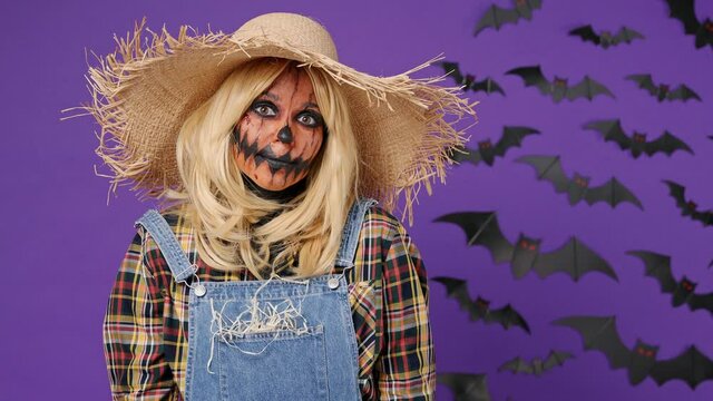Puzzled amazed young woman with Halloween makeup mask wear straw hat scarecrow costume look camera shrugging isolated on plain dark purple background studio portrait. Celebration holiday party concept