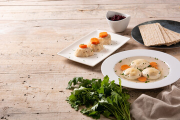 Traditional Jewish matzah ball soup, gefilte fish and matzah bread on wooden table
