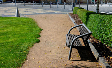 in the park there are hedges of evergreen shrubs. benches stand along the sidewalk in the square....