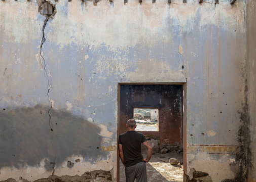 Rear view of adult man standing in doorway of an abandoned house