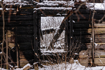 Old abandoned house burnt building in snow. Charred wooden walls and window are all what is left from home after accident with fire at winter day