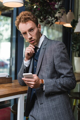 young businessman in formal wear and glasses holding smartphone in cafe