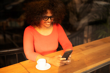 Young woman at cafe drinking coffee and using mobile phone. Beautiful African woman typing a message.