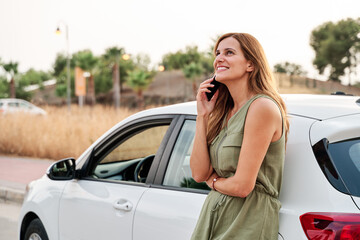 Young pretty woman standing leaning against her car while talking on her smartphone. - 456162172