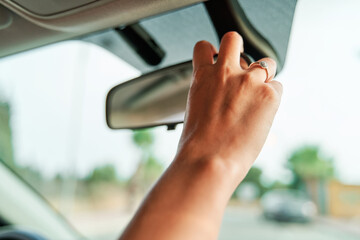 Close-up detail shot of an unrecognizable woman's hand adjusting the rearview mirror inside the car. - 456162199