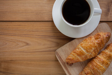 cup of coffee,  a laptop and croissant on a wooden table.