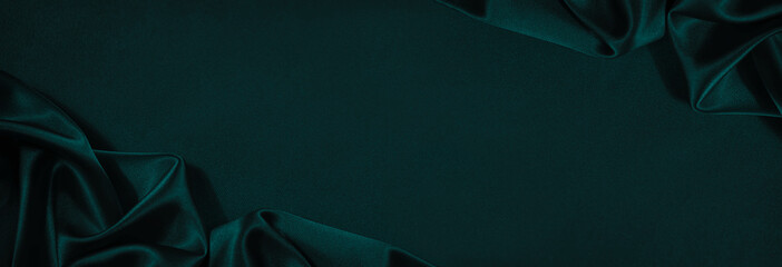 Dark blue green silk satin background. Beautiful soft folds on the smooth surface of the fabric....
