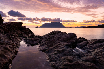 (Selective focus) Stunning view of the silhouette of Tavolara island during a dramatic sunrise with sone granite rocks in the foreground. Porto Istana, Sardinia, Italy.
